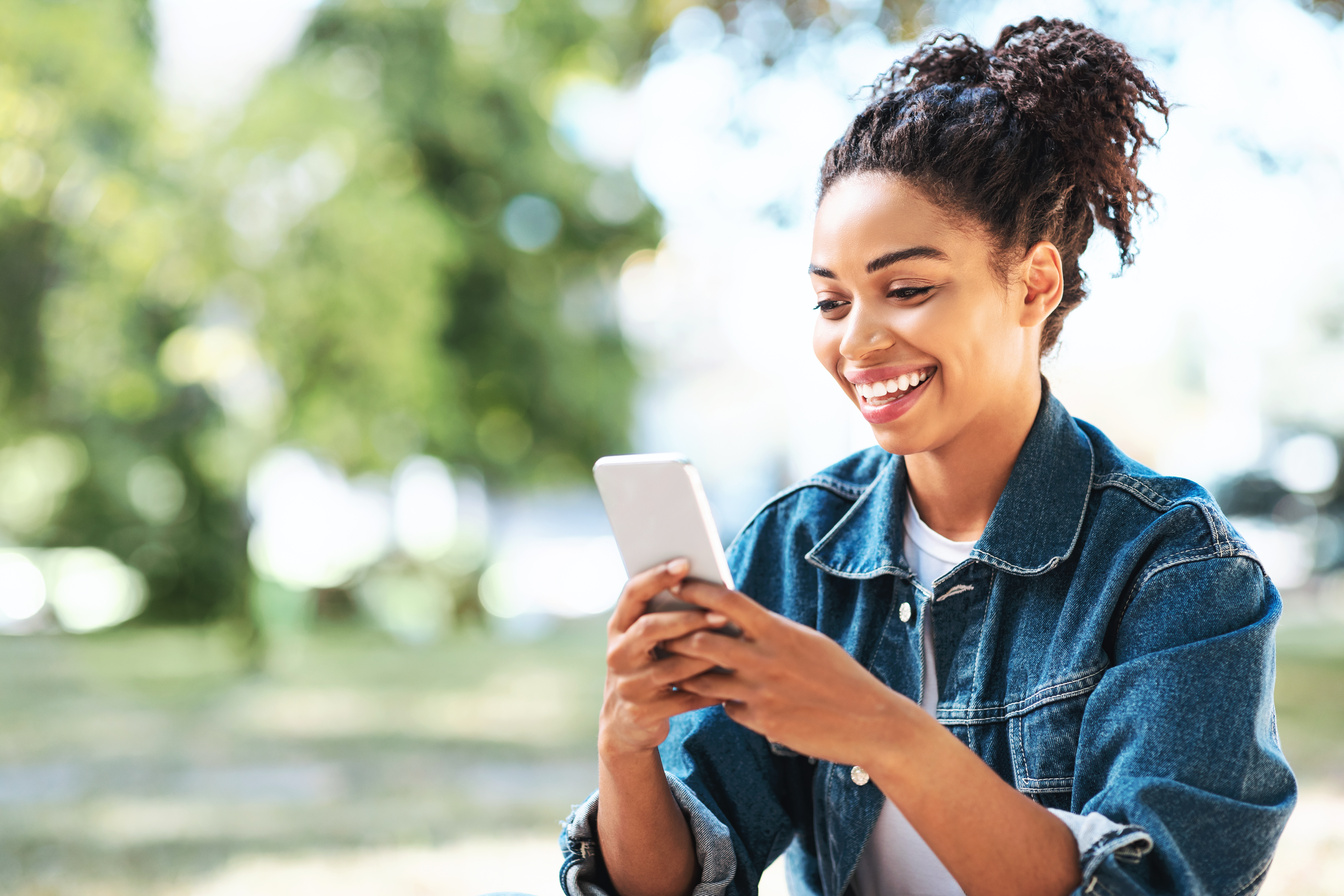 Happy Black Girl Using Mobile Phone App Sitting Outside